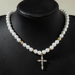Détail du collier de perles avec pendentif croix dorée et cristaux sur buste noir