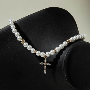 Détail d'un collier de perles blanches avec pendentif croix dorée et cristaux sertis
