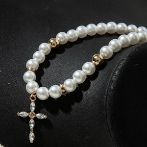Détail d'un collier de perles avec pendentif croix dorée incrusté de cristaux fins