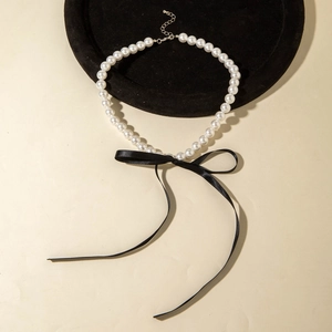 Detailed view of pearl necklace with black silk bow on a velvet display tray