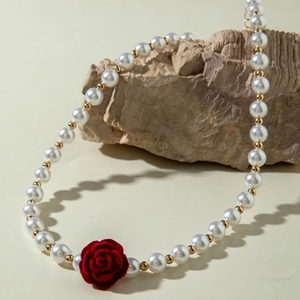 Close-up of pearl necklace featuring a red velvet rose detail on textured stone