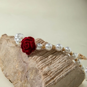 Detail of vintage pearl necklace featuring a red velvet rose and gold accent beads