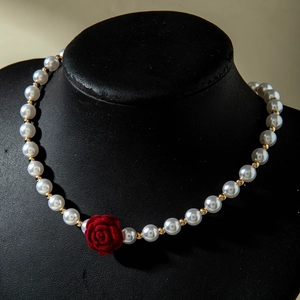 Close-up of elegant pearl necklace featuring a velvet red rose pendant and gold accents