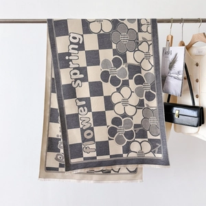 Close-up of checkered knit scarf with flower pattern and fringe detail on hanger