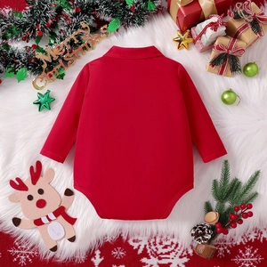 Flat lay of a red long-sleeve baby romper with collar on a plush rug with Christmas decor