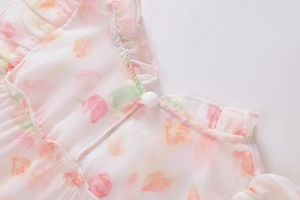 Detail eines geblümten Chiffonkleides mit Rüschenausschnitt und weißem Kugelknopf