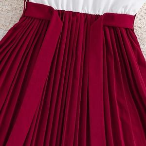 Detail of girls' dress showing waist belt, red pleated skirt, and white fabric texture