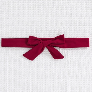 Close-up of a wine red vintage knit bow headband on white textured fabric background