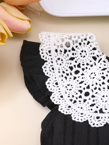 Close-up of intricate white floral lace detailing on a black girls' pleated dress fabric