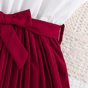 Detail of red pleated girls' dress featuring a large waist bow and academic style design