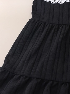 Detail of girls black pleated dress with white floral lace collar and ribbed texture