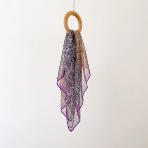 Détail d'un foulard en soie à motif paisley violet drapé dans un anneau en bois