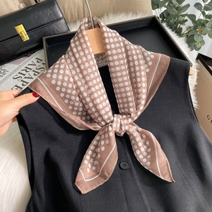 Détail d'un foulard en soie marron à pois noué sur une veste noire avec accessoires de mode
