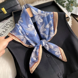 Détail d'un foulard en mousseline bleu ciel à fleurs attaché sur un gilet noir et bordure