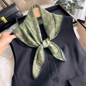 Detail of vintage green floral silk scarf styled on a black vest with lifestyle props