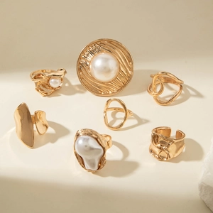 Lot de 7 bagues dorées géométriques avec perles et textures lave sous une lumière chaude
