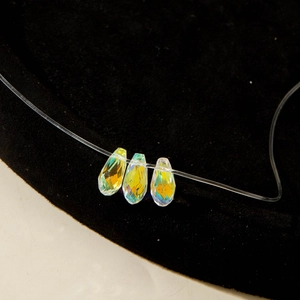 Détail de trois cristaux en goutte irisés sur un collier en fil de pêche invisible