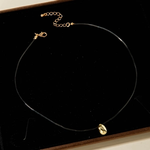 Détail d'un collier pendentif haricot doré sur un plateau de boîte à bijoux en velours noir