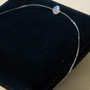 Gros plan sur un collier invisible minimaliste avec une perle aux reflets irisés