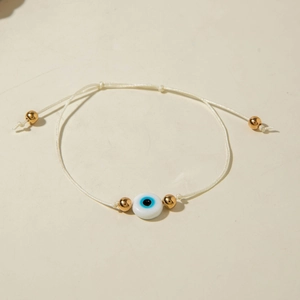 Detailed close-up of a white braided Evil Eye bracelet with gold beads and pull-string adjustment