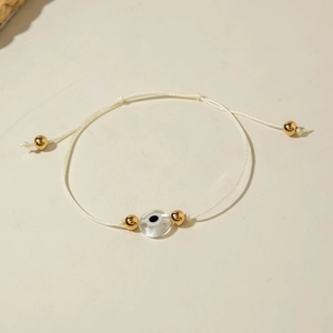 Detail of white woven Evil Eye bracelet with gold beads and protective amulet charm