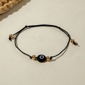 Detail of adjustable black cord bracelet with blue evil eye bead and golden accents