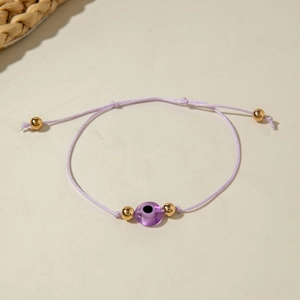 Detail of purple woven evil eye bracelet with gold beads on a minimalist background
