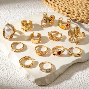 Detailed set of 12 gold baroque pearl and geometric flower rings on stone background