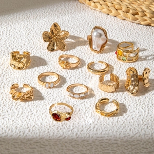 Detailed flat lay of gold baroque pearl rings and floral gemstones on a textured surface