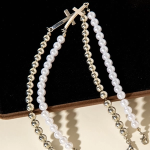 Detailed view of layered necklace featuring white pearls and metallic beads with cross pendants