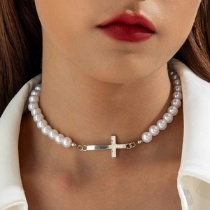 Macro detail of cross pendant and white pearls on a minimalist choker necklace