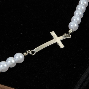 Macro shot of white pearls and polished silver cross pendant on black velvet background