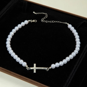 Detailed macro view of white round pearls with a silver horizontal cross pendant on a black base
