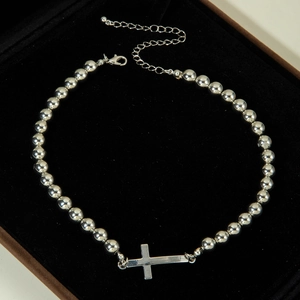 Detail of silver beaded necklace with horizontal cross pendant on black velvet padding