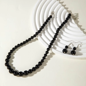 Detail of dark beaded necklace and earring set on white textured stone background