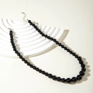 Polished black beaded necklace with silver adjustable chain on a white geometric stand