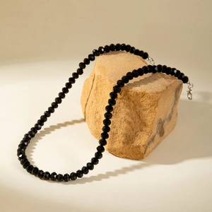 Close-up of black faceted beads necklace with silver lobster clasp on a natural stone base