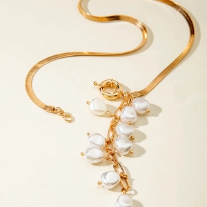 Detailed shot of golden snake chain necklace featuring a white faux pearl cluster pendant