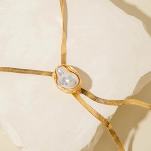 Detailed view of baroque pearl pendant on gold snake chain against a stone background