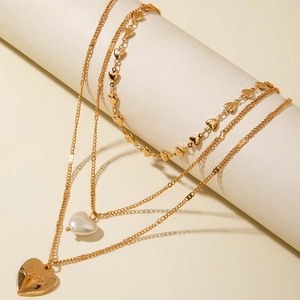 Collier doré à trois rangs avec pendentifs en cœur et perle blanche sur un présentoir