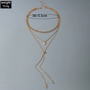 Détail macro du collier multi-rangs doré avec pendentif cœur et longue chaîne à pompon