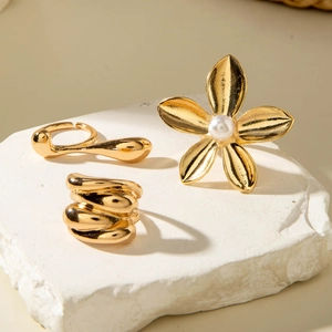 Gold plated ring set with flower pearl design and irregular textured bands on stone surface