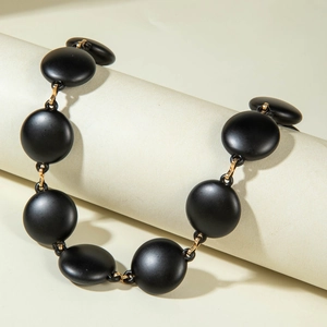 Close-up of matte black acrylic discs linked with gold rings on a necklace