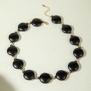 Detail view of a chunky black acrylic disc necklace with gold-toned metal links.