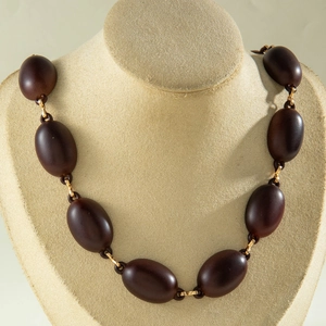 Detailed view of large oval dark brown acrylic beads connected by golden metal rings