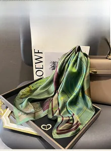 Détail d'un foulard en soie verte avec imprimé d'art sur un plateau et un sac