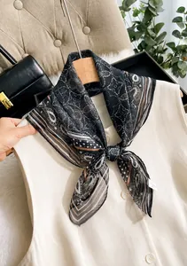 Detail eines schwarz-weißen Paisley-Seidenschals an einer beigen Weste in edlem Interieur