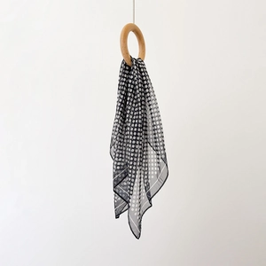 Detailansicht eines leichten schwarz-weißen Polka-Dot-Chiffonschals durch einen Holzring