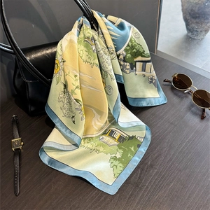 Elegant silk scarf with landscape print and blue border draped on a designer handbag