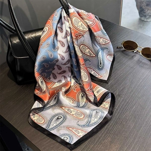 Elegant silk paisley square scarf with vibrant blue and orange patterns on black leather bag